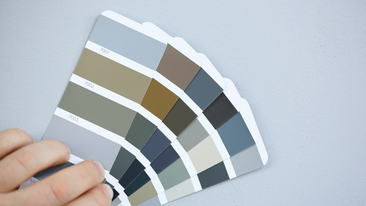 A hand holds multiple paint chips against a light blue wall.