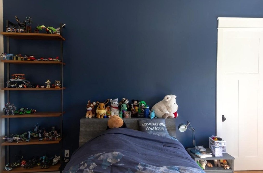 A bed with stuffed animals on it and a blue wall.