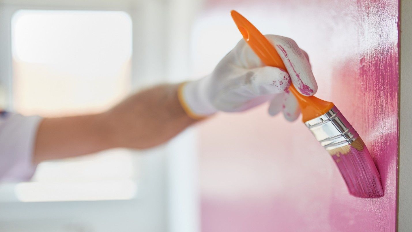 A painter uses a medium brush to paint a wall pink.